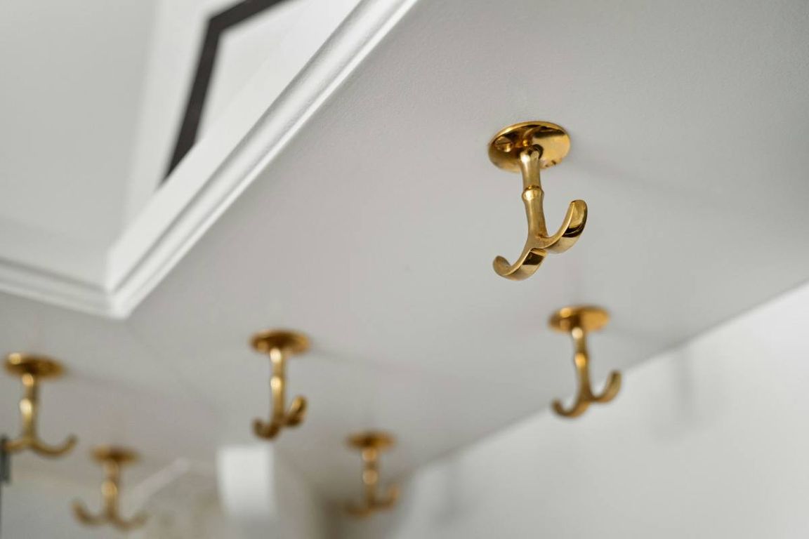 Several gold double hooks fixed on a white wall, one of them in sharp focus in the foreground.